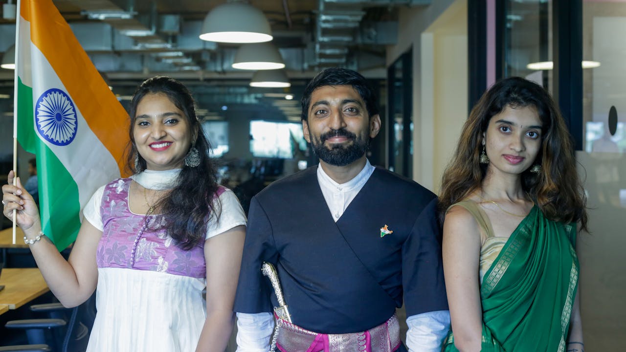 Three adults in Indian traditional dress holding the Indian flag in a modern office setting.